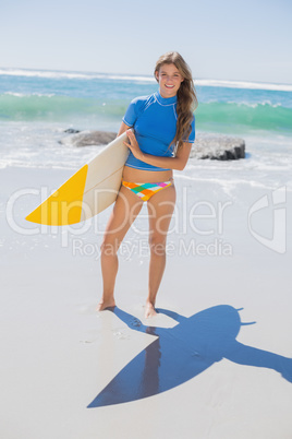 Fit smiling surfer girl on the beach with her surfboard