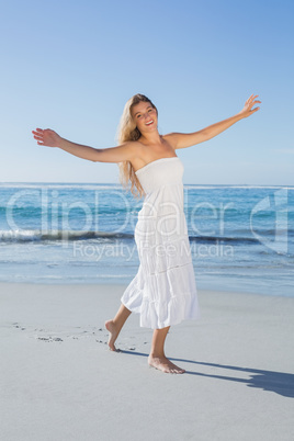 Beautiful blonde in white sundress on the beach smiling at camer