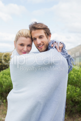Cute smiling couple standing outside wrapped in blanket
