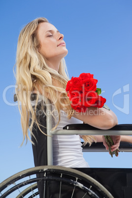 Wheelchair bound blonde smiling on the beach holding roses
