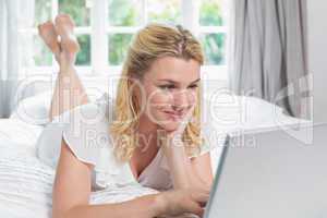 Pretty blonde lying on bed using laptop