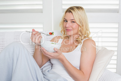 Happy blonde relaxing on the couch eating a salad