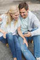 Hip young couple looking at smartphone sitting on skateboard