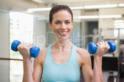 Fit brunette lifting blue dumbbells