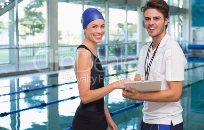 Swimmer smiling at camera with her coach by the pool