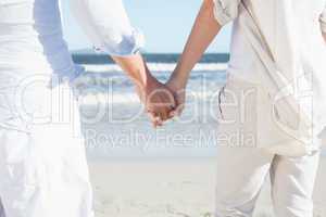 Couple on the beach looking out to sea holding hands