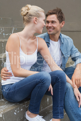 Hip young couple sitting on steps smiling at each other