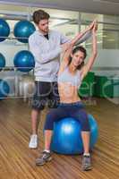 Trainer helping his client stretch on exercise ball