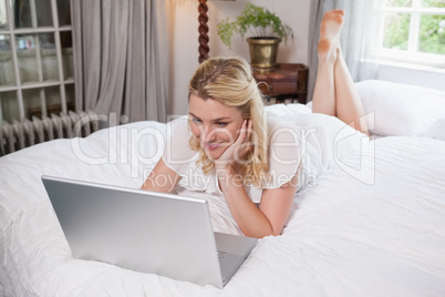 Pretty blonde lying on bed using laptop