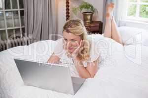 Pretty blonde lying on bed using laptop