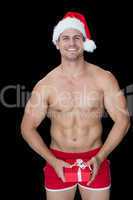 Smiling muscular man posing in sexy santa outfit holding gift