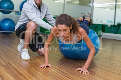 Trainer helping his client doing push up on exercise ball