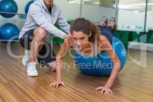 Trainer helping his client doing push up on exercise ball