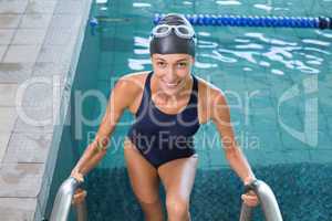 Fit swimmer smiling at camera getting out of the swimming pool