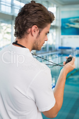 Swimming coach standing by the pool looking at stopwatch