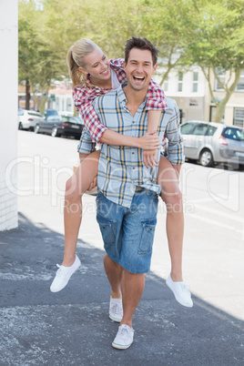 Young hip man giving his blonde girlfriend a piggy back