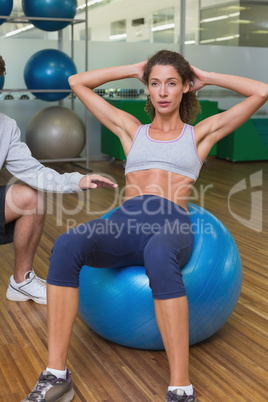Trainer helping his client doing sit up on exercise ball