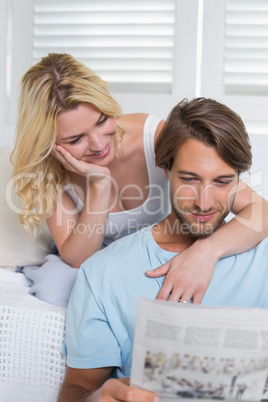 Happy casual couple sitting on couch reading newspaper together