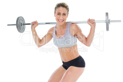 Smiling female crossfitter lifting barbell behind head looking a