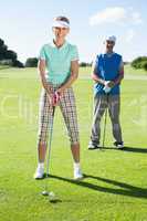 Smiling lady golfer teeing off for the day watched by partner