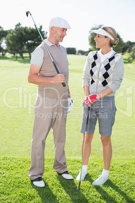 Golfing couple smiling at each other holding clubs