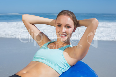 Fit woman lying on exercise ball at the beach doing sit ups