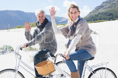 Carefree couple going on a bike ride on the beach waving at came