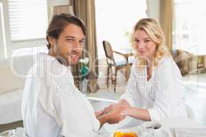 Cute couple in bathrobes having breakfast together holding hands