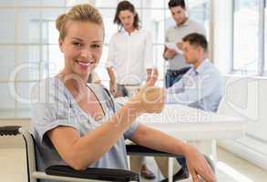 Casual businesswoman in wheelchair smiling at camera with team b