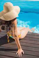 Beautiful brunette in bikini sitting by the pool paddling