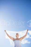 Pretty blonde in white dress holding up shawl on the beach