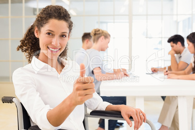 Casual businesswoman in wheelchair smiling at camera giving thum