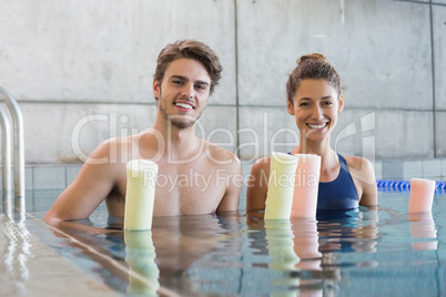 Man and woman standing with foam rollers in the pool