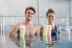Man and woman standing with foam rollers in the pool
