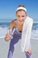 Sporty smiling blonde standing on the beach with towel and bottl