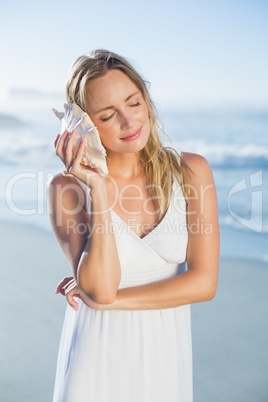 Pretty blonde standing at the beach in white sundress listening