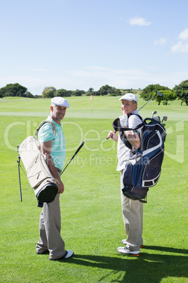 Golfer friends smiling at camera holding their golf bags