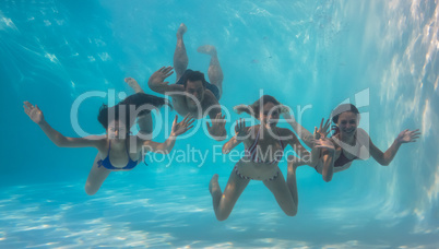 Smiling friends looking at camera underwater in swimming pool