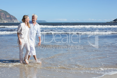 Happy couple walking barefoot on the beach