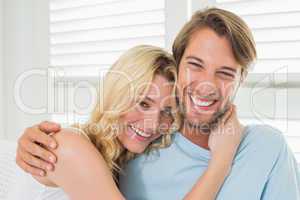 Cute casual couple sitting on couch laughing at camera