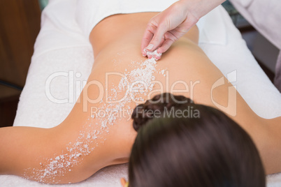 Beauty therapist pouring salt scrub on womans back