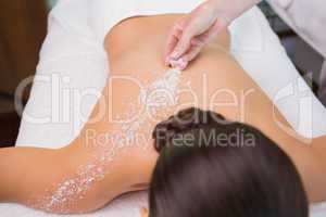 Beauty therapist pouring salt scrub on womans back