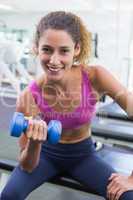 Pretty fit woman lifting blue dumbbell smiling at camera