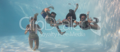 Smiling friends looking at camera underwater in swimming pool