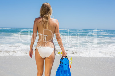 Fit woman in white bikini holding snorkeling gear on the beach