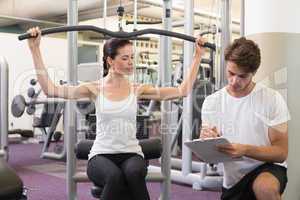 Fit brunette using weights machine for arms with trainer taking