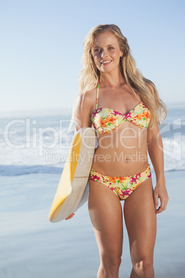 Gorgeous blonde surfer in bikini holding her board