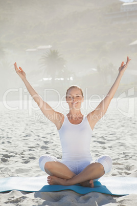 Smiling woman sitting in lotus pose on beach