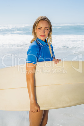 Blonde smiling surfer holding her board on the beach