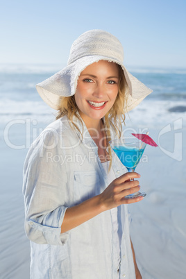 Smiling blonde relaxing by the sea holding cocktail